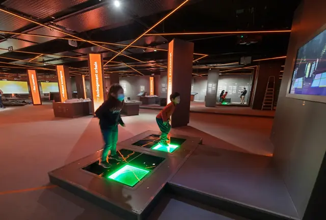 Two children stepping on separate illuminated floor platforms in a museum gallery.